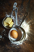 Butter, an egg, sugar and flour in measuring cups