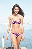 A brunette woman by the sea wearing a zig-zag patterned bikini