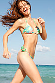 A brunette woman by the sea wearing a colourful bikini