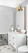 Bathroom washstand with marble top and brass fittings below mirror and wall lamps
