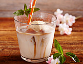 Almond milk with vanilla ice cream and coffee ice cubes in a glass with a straw and mint