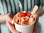 Rolled ice cream with strawberry in cone cup in woman hands