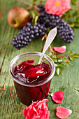 A jar of apple and grape jelly with rose petals with a silver spoon