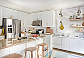 White kitchen with light wood accents, stainless appliances, brass hardware and white subway tiles