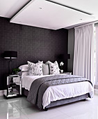 Doppelbett im Schlafzimmer mit glänzendem Fliesenboden, schwarzer Tapete und Deckenpaneel