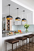 Breakfast bar, bar stools and black designer lamps in white kitchen