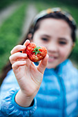 Mädchen hält herzförmige Erdbeere in der Hand