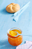 A jar of mango and vanilla jam with a bread roll