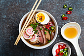 Cooking Japanese noodle soup ramen. Ramen with sliced pork, narutomaki, egg and kitchen spoon with broth on rustic stone background