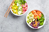 Top view of two assorted poke bowls with fresh raw tuna, salmon, vegetables, fruit