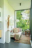 Statue of woman on plinth and couch next to glass wall