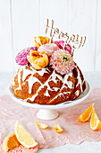Orange gugelhupf decorated with flowers and lettering saying 'Hooray'