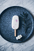 Creamy raspberry popsicle placed on dark dish on top of marble surface and decorated with flowers