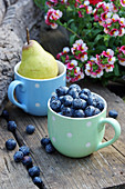 Blueberries and pear in mugs on wooden bench outdoors