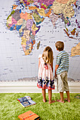 Zwei Kinder stehen vor einer Weltkarte