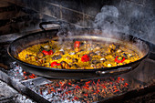 Hot delicious paella with rice, chicken and vegetables cooked in iron pan over open fire