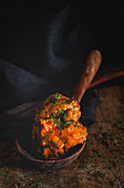 From above appetizing meatballs in brown wooden ladle on black striped towel