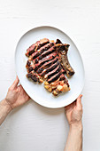 Hands holding rib steak served with potato on white background