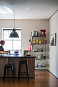 Island counter with bar stools, industrial lamps and metal shelves: woman next to window