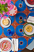 Rot und blau gemusterte Tischdecke und Tischsets, Keramikteller mit Törtchen