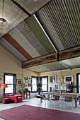 Rustic wooden table, red armchair and dining area in open-plan interior with corrugated metal roof