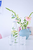 Flowers in pale blue vase, bottle of water and drinking glasses on dining table