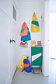 Small locker and brightly coloured cloth bags on hooks in white-tiled niche