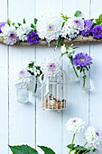 Small bottles and cage holding dahlias and asters suspended from branch