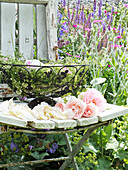 Alter Gartenstuhl mit Fensterrahmen, Metallschale und Rosenblüten