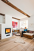 Helles Wohnzimmer mit Holzboden und Kamin, Frau auf Sofa sitzeend