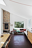 Seating area below window and next to brick fireplace in summerhouse with sloping ceiling