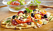Grilled pizza topped with sausage, feta cheese, olives, peppers and fresh herbs