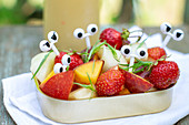 Summer fruit and berry salad in a jar with funny cartoon eyes picks