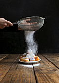 Cook sieving sugar powder on top of tasty biscuits