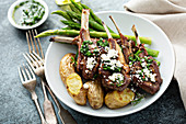 Grilled lamb chops with green herb sauce, feta, asparagus and potatoes served on a wooden board