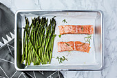 Salmon and asparagus in the pan, ready for oven, seasoned with olive oil and rosemary