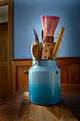 Kitchen utensils in a blue milk can on a rustic wooden table
