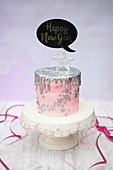 A New Year's Eve cake with sliver drips and a decorative speech bubble