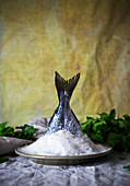 Body of fresh raw fish placed in heap of salt near parsley against yellow drapery