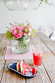 Watermelon, lemonade and vase of garden flowers on wooden table