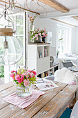 Bouquet of summer flowers on dining table and shabby-chic living room in background
