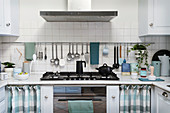 Utensils hung from rod on white-tiled wall above kitchen counter