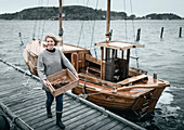 Smiling woman carrying lobsters, boat on background