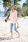 A brunette woman on the beach wearing a wide tunic and denim capri trousers
