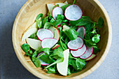 Lambs lettuce with apple and radish slices in a wooden bowl