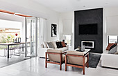 Sofas and armchairs in front of fireplace and TV on black wall in bright interior