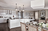 U-shaped kitchen counter with bar stools below pendant lamps and dining area in foreground of bright kitchen