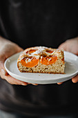 A hand holding a slice of apricot cake on a plate