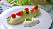 Stuffed crepes with cream, strawberries and raspberries being made