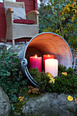 Three pillar candles in zinc bucket lying on side in garden